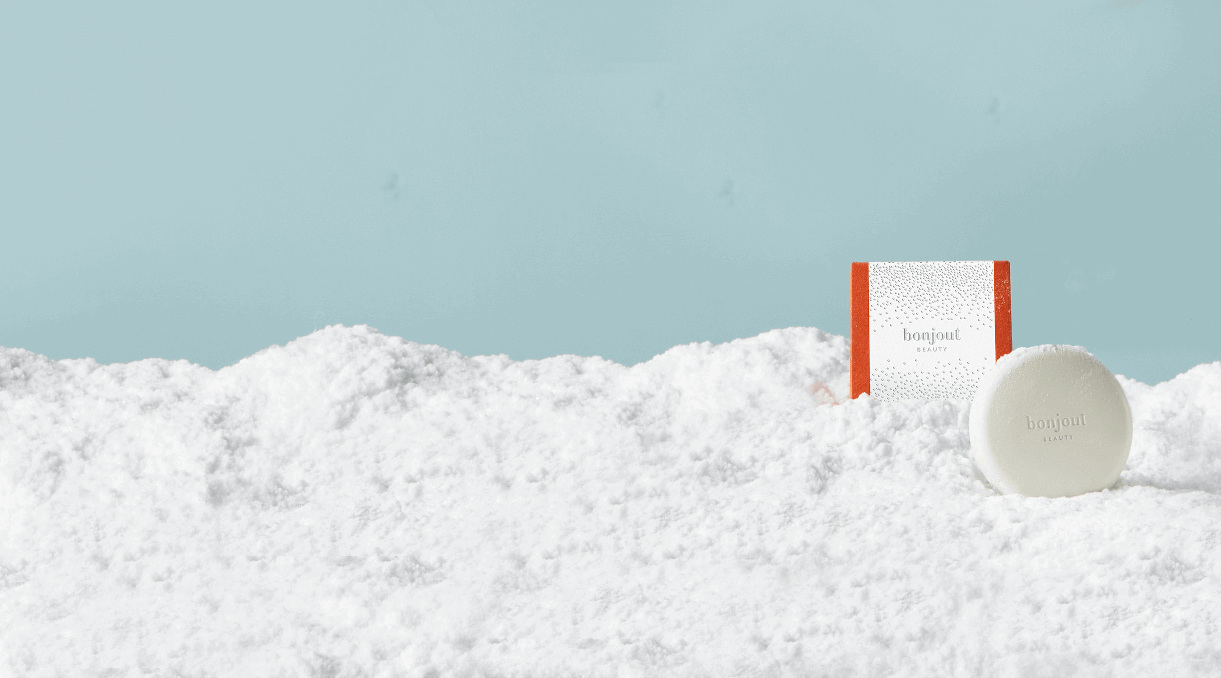 Bonjout Beauty's Le Balm Product next to Holiday Packaging surrounded by snow