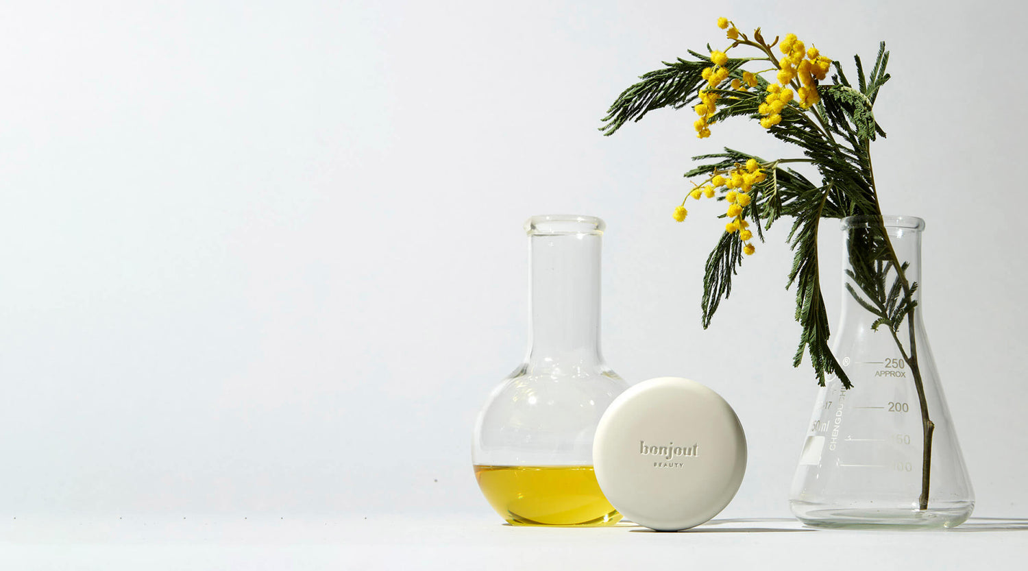 Bonjout Beauty's Le Balm product with beaker filled with oil and yellow flowers